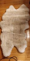 Full view of light cream sheepskin rug on hardwood floor showing soft wool texture and organic natural shape
