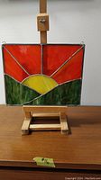 Front view of stained glass panel showing sunset scene on wooden easel.