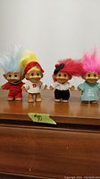 Four vintage Russ troll dolls displayed side by side on a wooden surface, showing colorful hair and various outfits.
