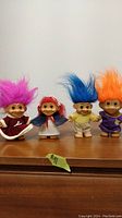Four vintage troll dolls placed in a row on a wooden surface, showing different hair colors and outfits.