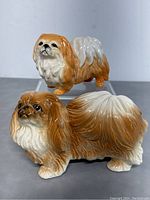 Two porcelain dog figurines placed on a clear stand, showing size difference and color details.