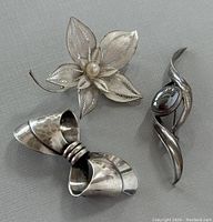 Full view of the three brooches with floral, bow, and abstract designs showing overall condition and details.