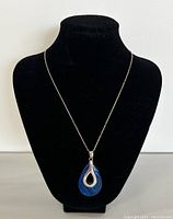 Full front view of necklace on black display bust showing silver chain and teardrop blue shell pendant with silver overlay.