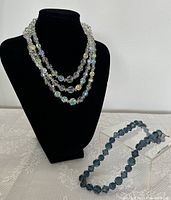 Photo showing both necklaces displayed on black necklace bust and clear riser.