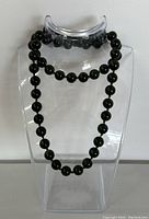 Full front view of dark green jade bead necklace displayed on a clear stand, showing the length and bead arrangement.