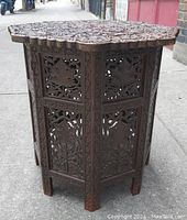 Photo of assembled handcrafted teak folding table showing detailed floral carvings and scalloped edges.