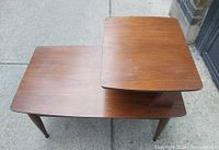 View of the end table showing the smaller upper shelf offset over the larger bottom shelf with smooth walnut wood finish.