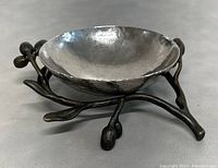 Close-up image of the Michael Aram olive branch bowl showing the hand-hammered stainless steel surface and the olive branch designed metal base with twig and olive details.