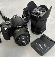 Front view of Nikon D40X body with 18-55mm lens attached, 18-200mm lens and Nikon MH-23 charger alongside