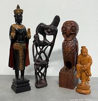 Photo showing four wooden sculptures including Thai Buddha statue, Makonde art figure, wooden owl, and small carved figurine.