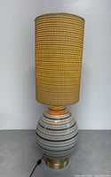 Front view of the pottery table lamp showing the striped ceramic base and woven shade.