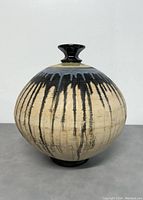 Front view of signed pottery globe vase with beige body and black drip glaze.