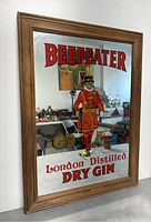 Front angled view of rectangular wood framed advertising mirror featuring Beefeater London Distilled Dry Gin text and image of Yeoman Warder in red uniform.