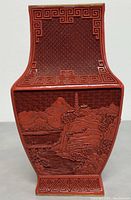 Front view of vase showing carved mountain landscape panel and fret border