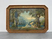 Full view of framed art deco print measuring 21.5x13.5 inches featuring a reclining woman holding a baby outdoors by trees and water with mountains in the background