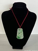 Jade pendant displayed on a black necklace holder showing the carving and red cord.