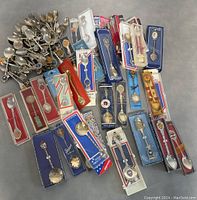 Top view of collection of vintage souvenir spoons, many in original packaging laid out showing various designs and packaging colors