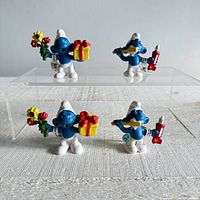 Front view of four vintage Schleich Smurf figurines showing two Gift Smurfs with flowers and gifts, and two Smurfs with Toothpaste holding toothpaste tube and trumpet.