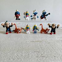 Front view of all 11 PVC Smurf and related character collectible figurines arranged in two rows on acrylic display stands, showing paint details, tags, and relative sizes.