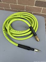 Coiled yellow-green air hose on table with brick background.