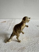 Side view of the vintage brass Ceratosaurus dinosaur figurine showing its profile, tail, and clawed feet.