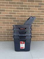 Stack of five dark blue Rubbermaid storage bins with one lid propped up inside the top bin to show matching lids.