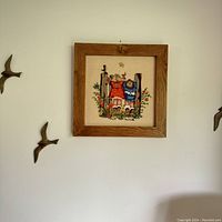 Overall image of framed embroidered art hanging on wall with decorative bird wall hangings