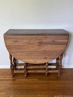 Front view of the gate leg table with one drop side folded down, showing wood grain and drawer front.