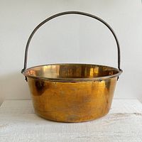 Front side view of large brass bucket with handle showing its shape and patina.