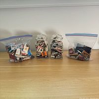 Two glass jars filled with matchbooks and two Ziploc bags with additional matchbooks displayed on a wooden surface against a white wall.