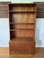 Full frontal image of mid century modern wall unit showing bookshelf portion with four shelves and lower drawers.