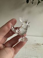 Crystal chicken figurine held in hand showing details of the faceted body, frosted comb, black eyes, and clear feet and tail.