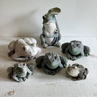 Photo showing all six resin garden frog figurines arranged in two rows on a light-colored surface.
