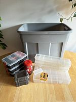 Large grey Rubbermaid storage bin with legs and various smaller storage organizers on table in natural light.