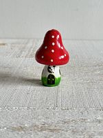 Front view of small red and white mushroom house figurine with small mouse detail at the door area.