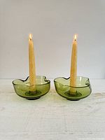 Pair of vintage avocado green glass candle holders holding lit taper candles showing color, shape and size.