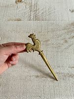 Hand-held vintage brass rooster letter opener showing size and detailed rooster design