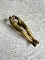 Image of vintage brass nutcracker shaped like woman's legs, showing overall view on a white textured surface.