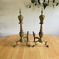 Pair of vintage brass fire andirons displayed on wooden table, showing overall design and size.