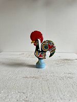 Front view of colorful ceramic rooster figurine with detailed painted patterns and red comb.