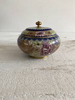Side view of the round cloisonne pot with lid closed, showing floral enamel design and brass finial.
