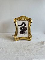 Front view of the vintage brass ornate frame holding the snake art print, showing details of frame design and art.