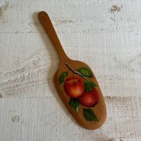 Top side of a wooden butter paddle showing hand-painted apples on a branch with leaves.