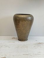 Front view of the large vintage brass vase showing geometric hammered designs and cylindrical shape tapering at the base.