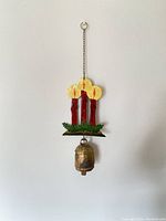 Full front view of vintage metal hanging candle decoration with large cow bell attached by a metal chain.