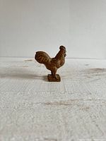 Front and side views of a small vintage painted metal chicken figurine paperweight, showing detailed texture and rustic brown paint.