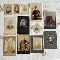 Top-down view of 13 vintage black and white and sepia photography portraits of men in formal attire, arranged on a fabric surface. Sizes range approximately 2 7/8" x 2 7/8" to 6.5" x 4.25".