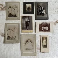Top-down view of eight vintage black and white and sepia photographs showing various children and family portraits mounted on different backgrounds.