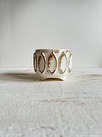 Front view of vintage white and gold pottery planter on pedestal with oval patterns and textured surface.