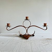 Front view of the copper candlestick holder showing three holders with looped arm design and triangular base.